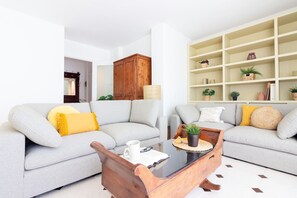 A living room with two grey sofas, a wooden coffee table, and a white wall with shelves.