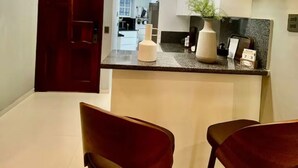 A modern kitchen with pendant lighting, a central island, and two red chairs. - Marcial Luxury Apartments - Apt 2A (Baní)