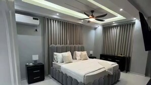 A modern bedroom with a large bed, a ceiling fan, and a built-in air conditioning unit. - Marcial Luxury Apartments - Apt 2A (Baní)