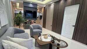 A modern living room with a grey sofa, a coffee table, and a TV mounted on the wall. - Marcial Luxury Apartments - Apt 2A (Baní)