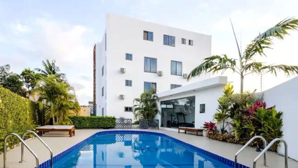 A modern building with a swimming pool, surrounded by greenery and palm trees. - Legacy Unit - Central Yet Serene - Pool & Fast WiFi (Plum)