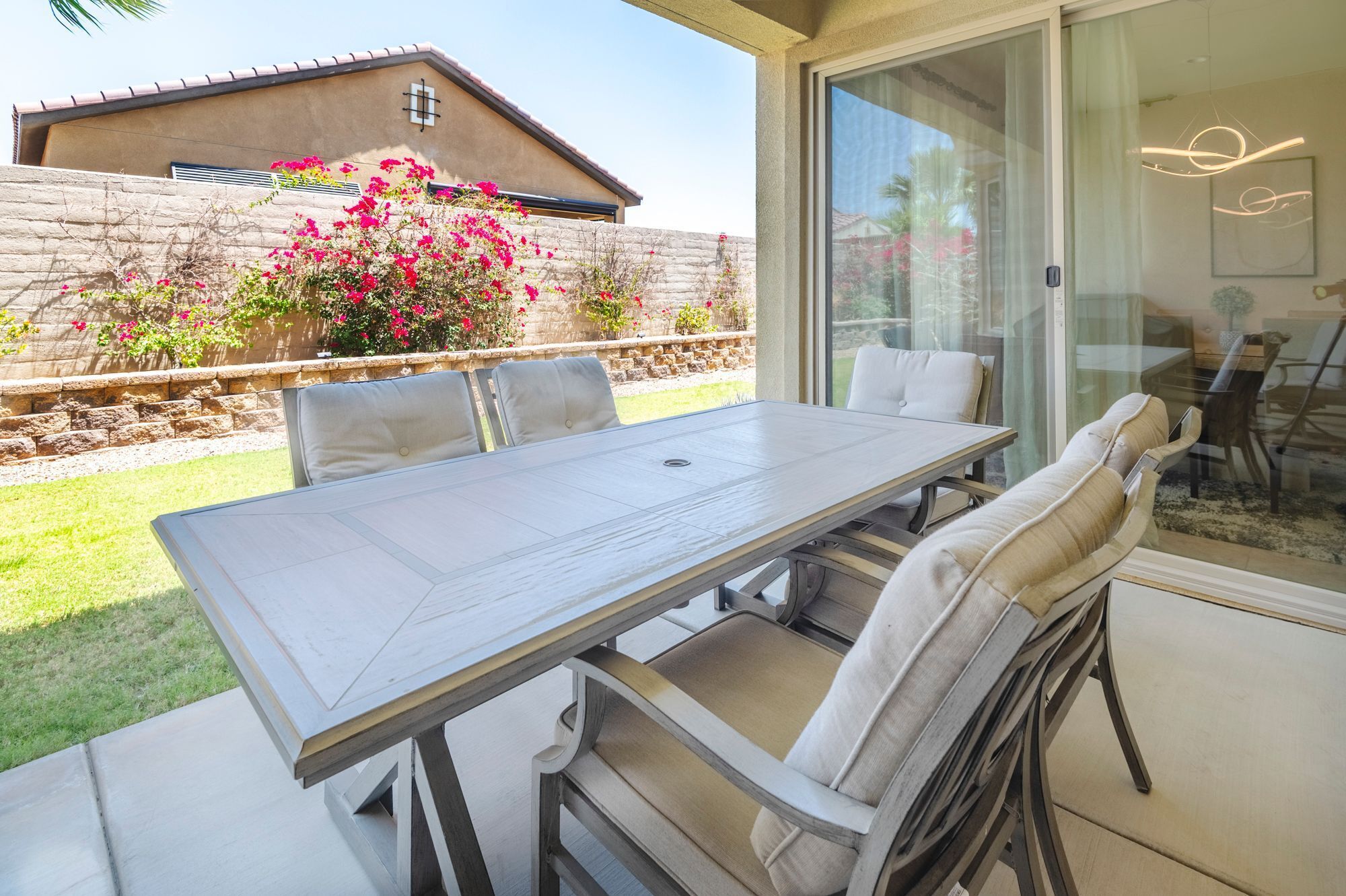 Une terrasse avec une table et des chaises, un mur en pierre et une maison en arrière-plan.