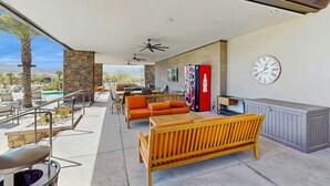 Uma área de estar coberta ao ar livre, com piscina, parede de pedra e um relógio na parede.