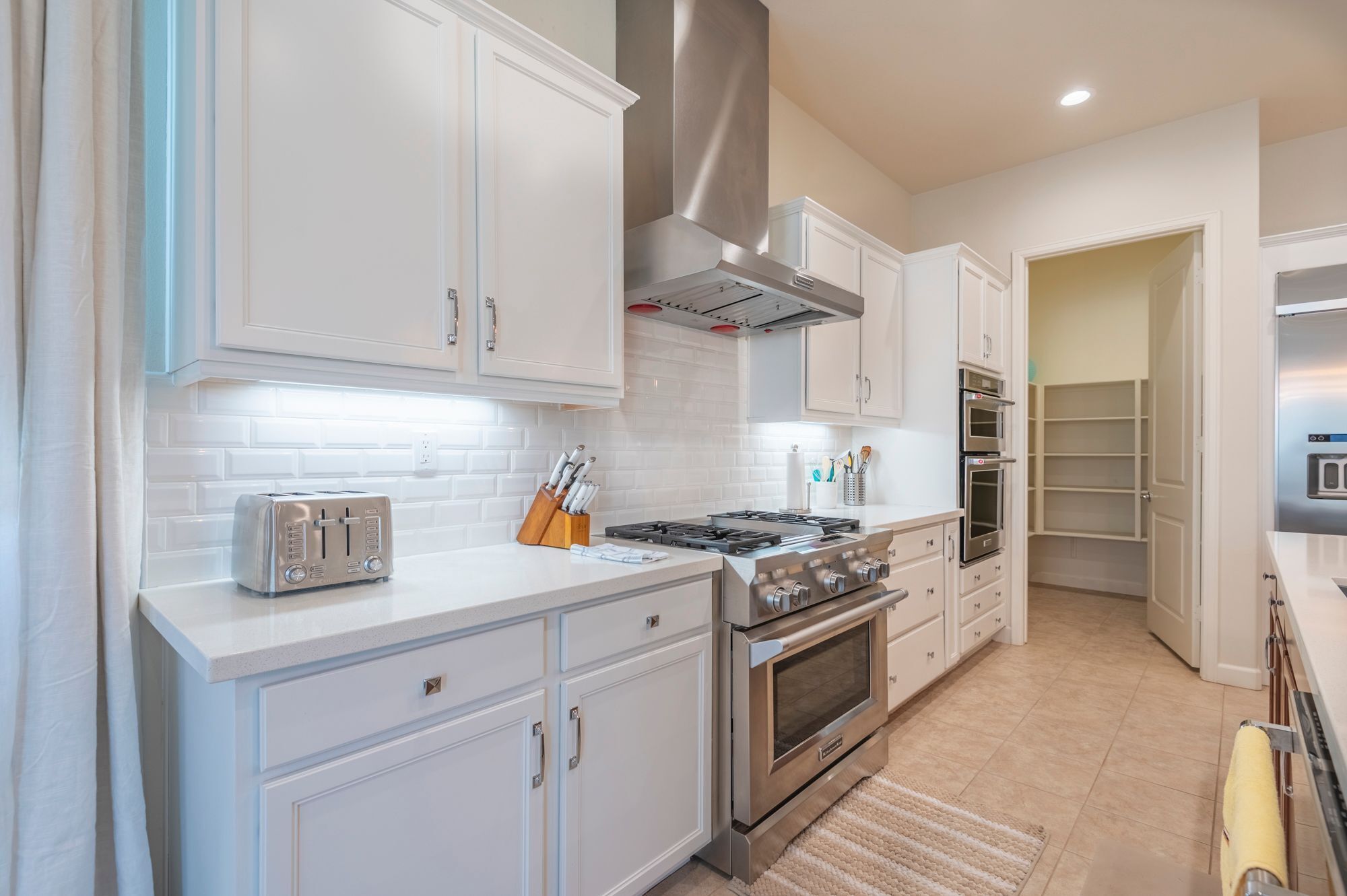 A modern kitchen with white cabinets, a gas stove, a built-in oven, and a toaster.