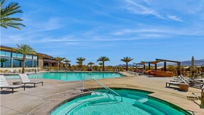 Uma área de piscina com espreguiçadeiras, uma banheira de hidromassagem circular e palmeiras.