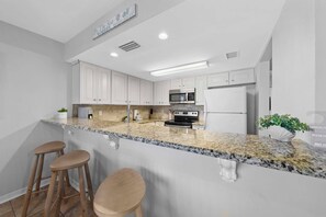 Eine Küche mit weißen Schränken, Granit Arbeitsplatten, einem Edelstahlkühlschrank und einer Mikrowelle.