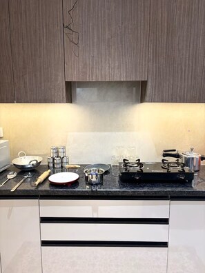 Una cocina con estufa a gas, hervidor, sartén y distintos utensilios.