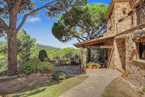 A stone building with a balcony, surrounded by trees and a stone pathway. - Villa 'Can Ayala' Arenys de Munt – With Garden and Private Pool. (Collsacreu)