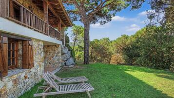 Un edificio rustico in pietra con un balcone affacciato su un prato curato e alberi.