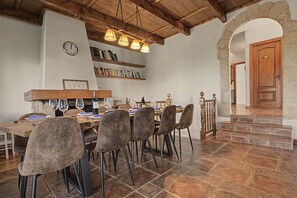 Un comedor con una mesa de madera, sillas e iluminación colgante. Hay estanterías sobre la mesa y un reloj en la pared.