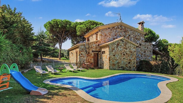 A stone house with a swimming pool, a slide, and a fenced garden area. - Villa 'Can Ayala' Arenys de Munt – With Garden and Private Pool. (Collsacreu)
