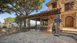 A stone building with a covered patio area, outdoor seating, and a basketball court. - Villa 'Can Ayala' Arenys de Munt – With Garden and Private Pool. (Collsacreu)