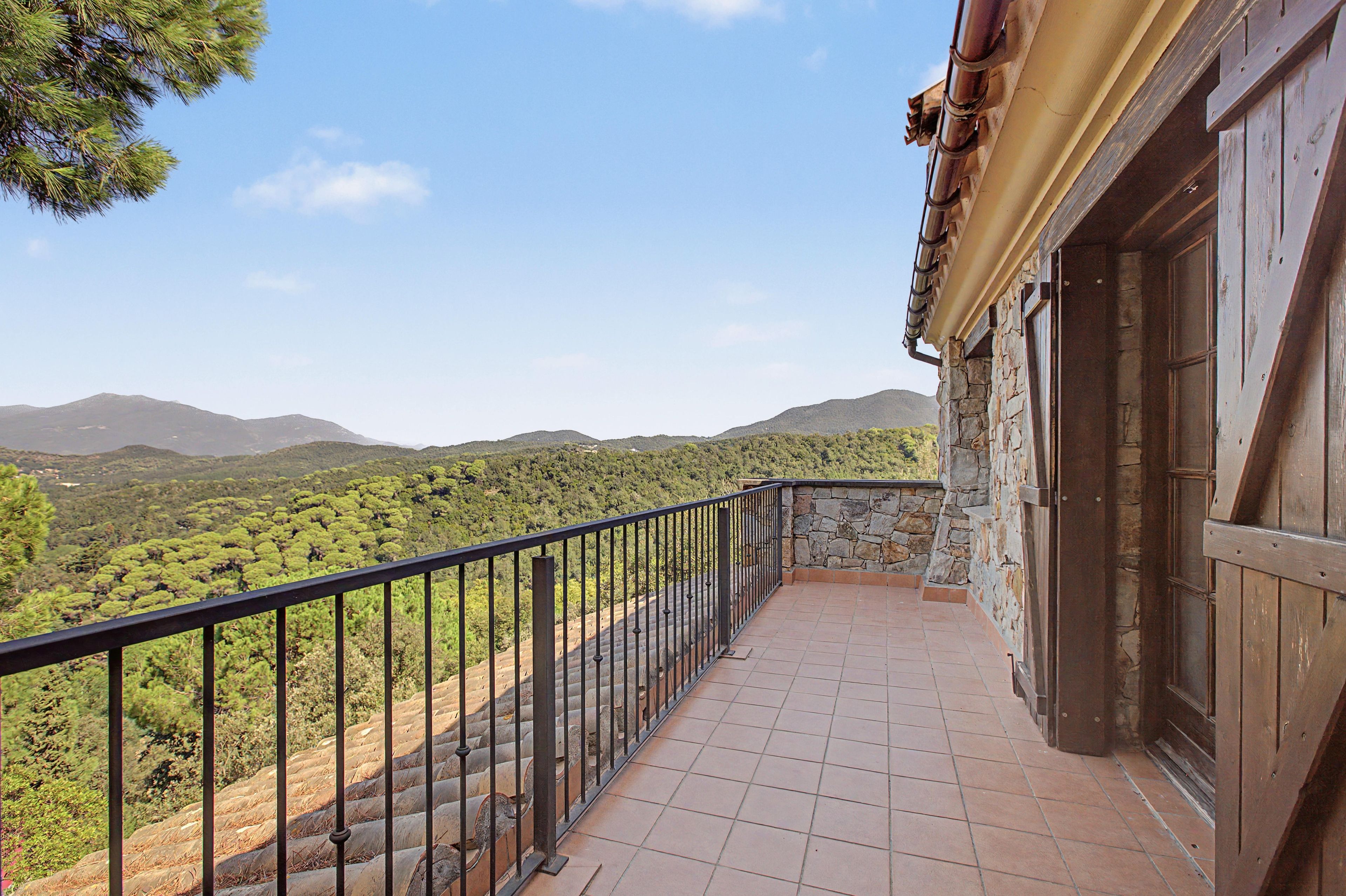A balcony with a stone wall and metal railing overlooking a mountainous landscape.