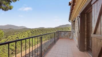 A balcony with a stone wall and metal railing overlooking a mountainous landscape.