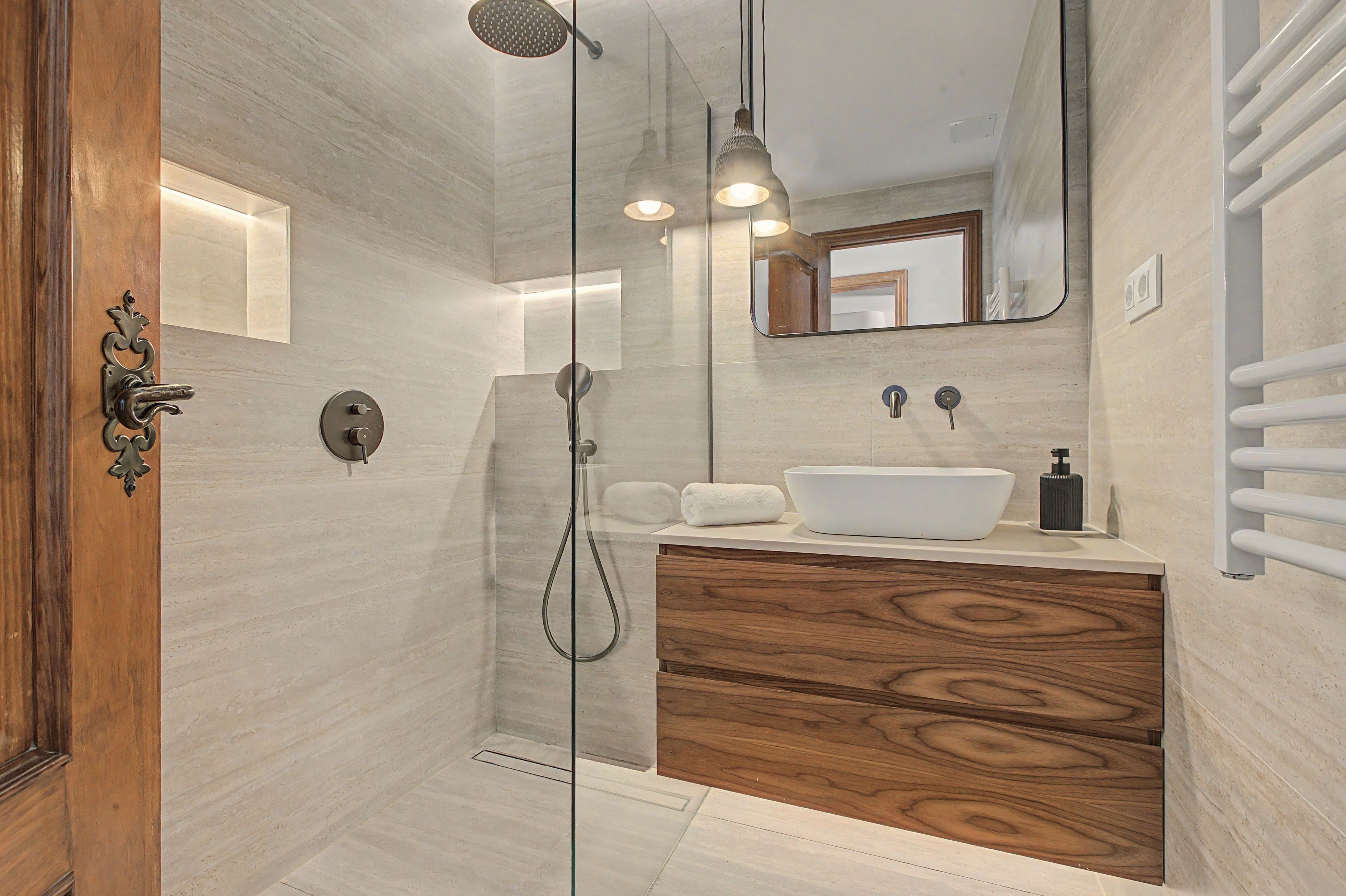 Un baño moderno con cabina de ducha de vidrio, tocador de madera, lavamanos blanco y una toalla.