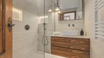 Un baño moderno con cabina de ducha de vidrio, tocador de madera, lavamanos blanco y una toalla.