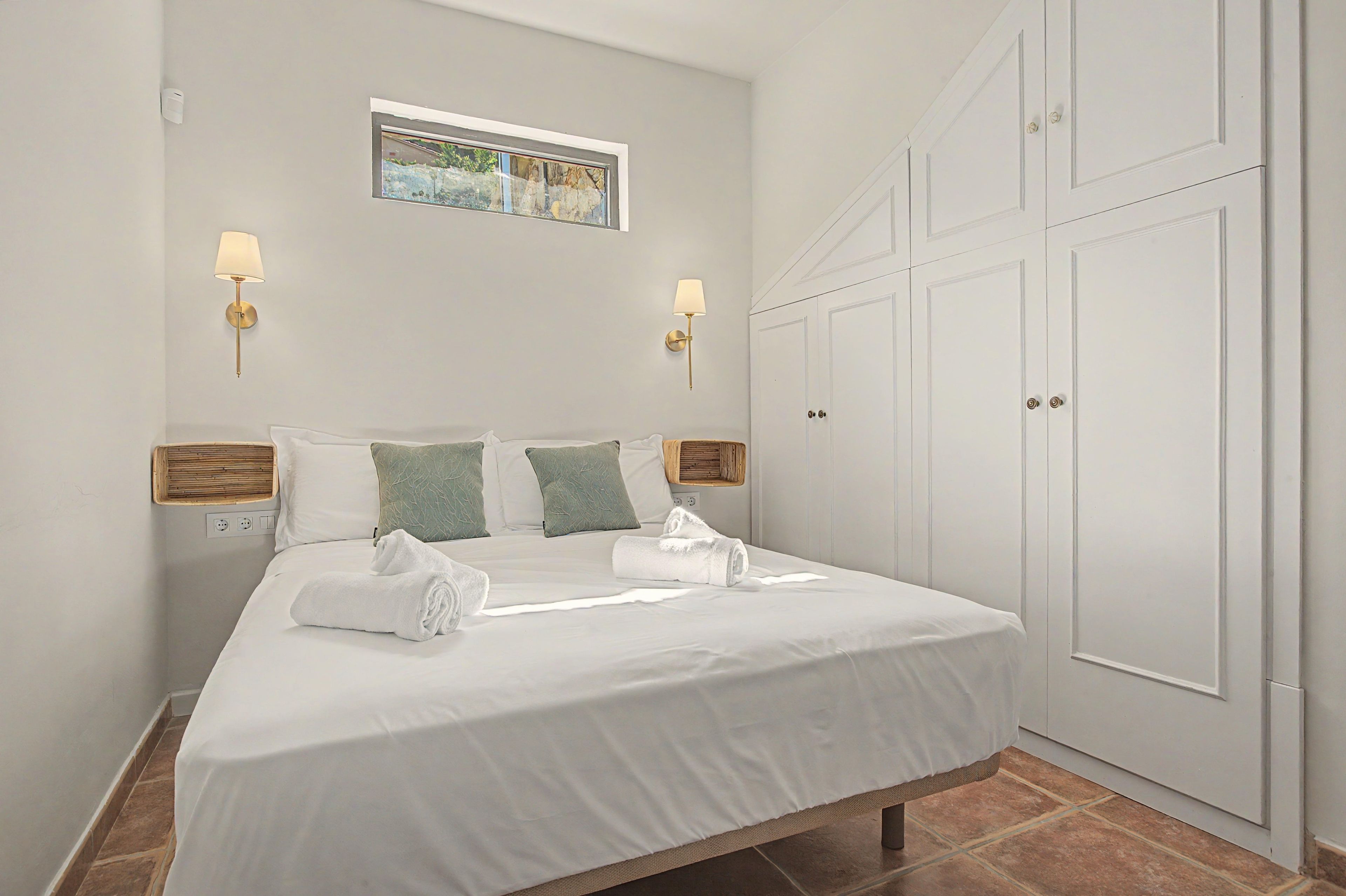 Een hotelkamer met een bed, twee wandlampen, een raam met een schilderij en een kledingkast.