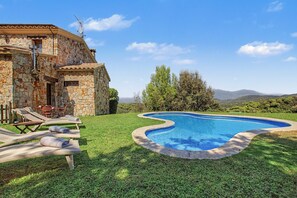 Una villa de piedra con piscina, zona de estar exterior y vistas a las colinas.