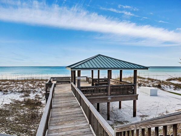 A wooden boardwalk leading to a beach gazebo with a metal roof. - Close to Beach, 2 Balconies, Community Pool (Miramar Beach)