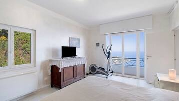 Un dormitorio con cama, cómoda, televisor, bicicleta estática y balcón con vistas.
