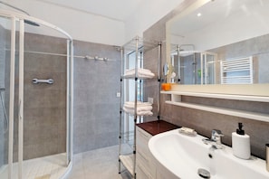 Un bany modern amb dutxa de vidre, un lavabo blanc amb mirall i una barra de tovalloles.