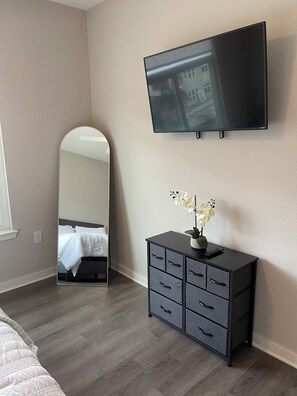 Quarto com cama, cômoda, televisão, espelho e janela.