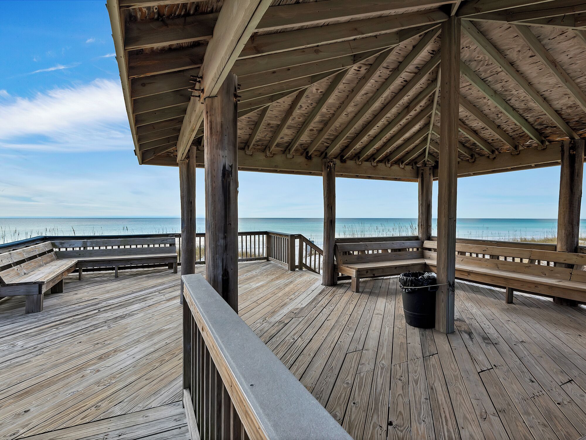 A wooden pier with benches and a railing overlooking a beach.