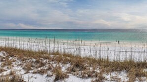 En strand med krystalklart turkis vand, hvidt sand og sparsom vegetation.