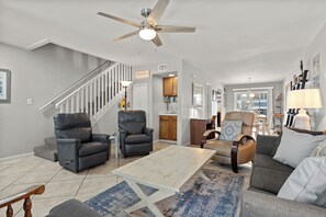A spacious living room with a high ceiling fan, a staircase, and a view into the kitchen. - Steps to the Beach, Private Balconies, Community Pool (Miramar Beach)