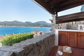 A stone wall, wooden shutters, a table with a tray, and a view of the sea and mountains. - Casa Matilde con Patio by Wonderful Italy (Olbia)