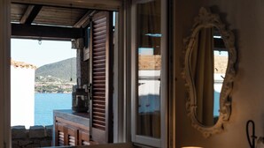 A room with a view of a body of water and hills, a wooden table, a lamp, and a mirror on the wall. - Casa Matilde con Patio by Wonderful Italy (Olbia)