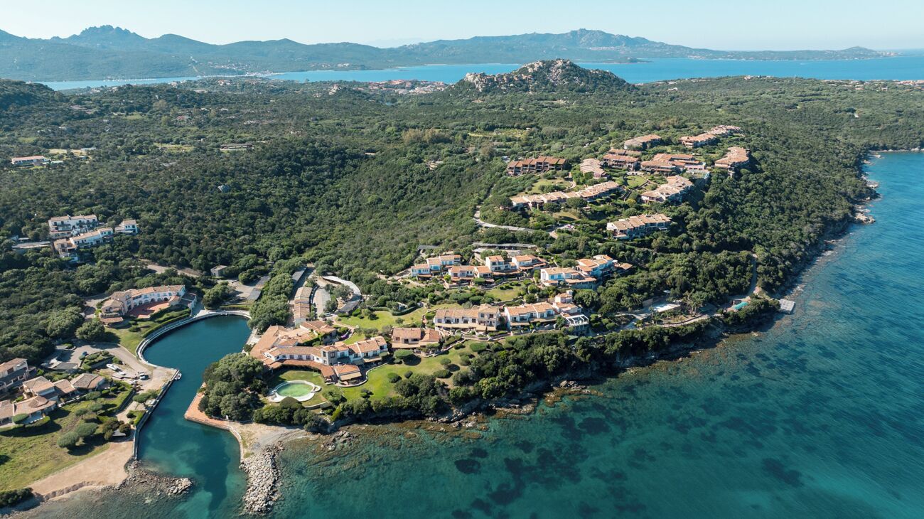 An aerial view of a coastal residential area with houses, a winding road, and a body of water.
