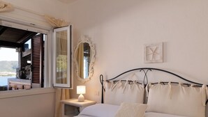 A bedroom with a bed, a nightstand, a lamp, a mirror, and a view of the outdoors. - Casa Matilde con Patio by Wonderful Italy (Olbia)