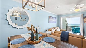 A dining area with a wooden table, blue placemats, a mirror, and a view of the ocean through large windows. - Beach Front Townhome in Miramar Beach (Miramar Beach)