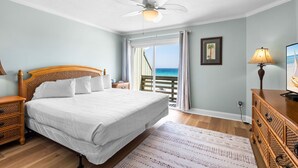 A bedroom with a bed, wooden headboard, nightstands, a dresser, a ceiling fan, a window with a view of the ocean, and a door leading to a balcony. - Beach Front Townhome in Miramar Beach (Miramar Beach)