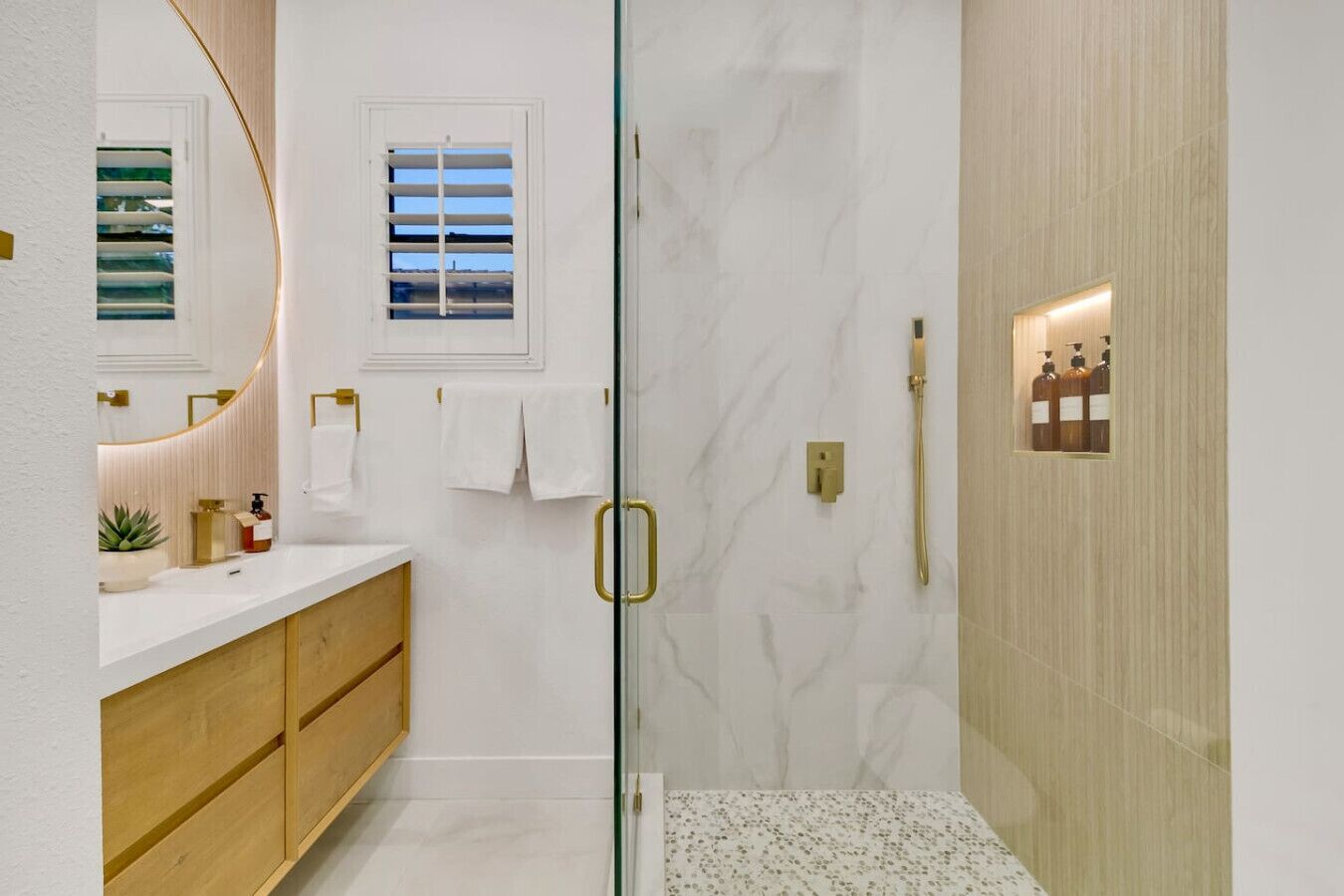 A bathroom with a glass shower enclosure, a wooden vanity, and a marble wall.