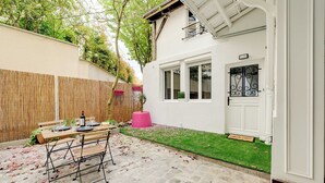 Um pátio com uma mesa posta para refeições, cerca de madeira e um edifício branco com uma porta.