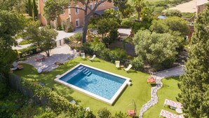 Una piscina envoltada per un jardí ben cuidat, un camí de pedra i un arbre gran.