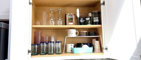 A kitchen cabinet with shelves containing glassware, coffee containers, and a blue dish rack.