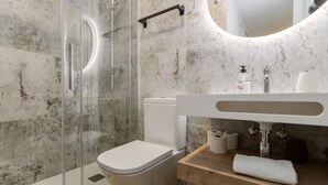 A bathroom with a glass shower enclosure, a white toilet, a wooden vanity with a sink, and a mirror above the vanity. - Txapitela Rooms - Perfect for 2 (Pamplona)