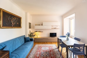 Ein Wohnzimmer mit Sofa, Fernseher, Esstisch, Stühlen und einem gemusterten Teppich.