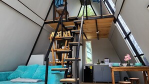 A loft-style room with a wooden staircase, a sofa, a table, and a kitchen area.
