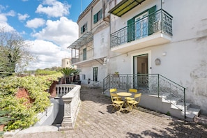 A courtyard with a stone staircase, a small outdoor table with chairs, and a building with balconies.