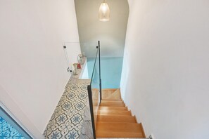 A staircase with patterned flooring leading to a room with a blue wall and a hanging light fixture.
