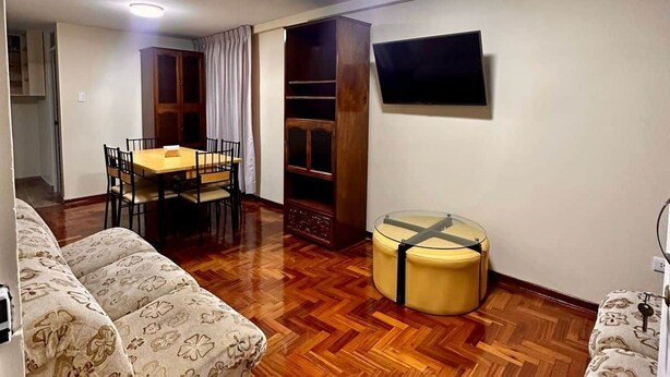 Un salon doté d’un parquet en bois disposé en motif « point de Hongrie », d’un canapé, d’une table à manger avec des chaises, d’un téléviseur fixé au mur et d’une bibliothèque intégrée.