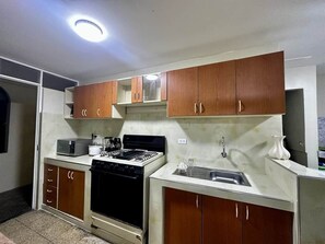 Una cocina con armarios de madera, estufa, microondas y pileta.