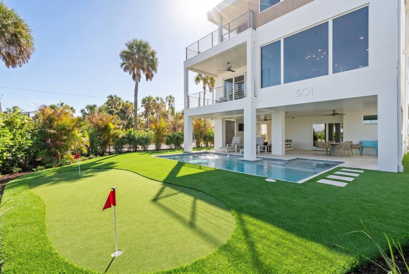 A modern two-story house with a swimming pool, a well-maintained lawn, and a flag on the putting green.