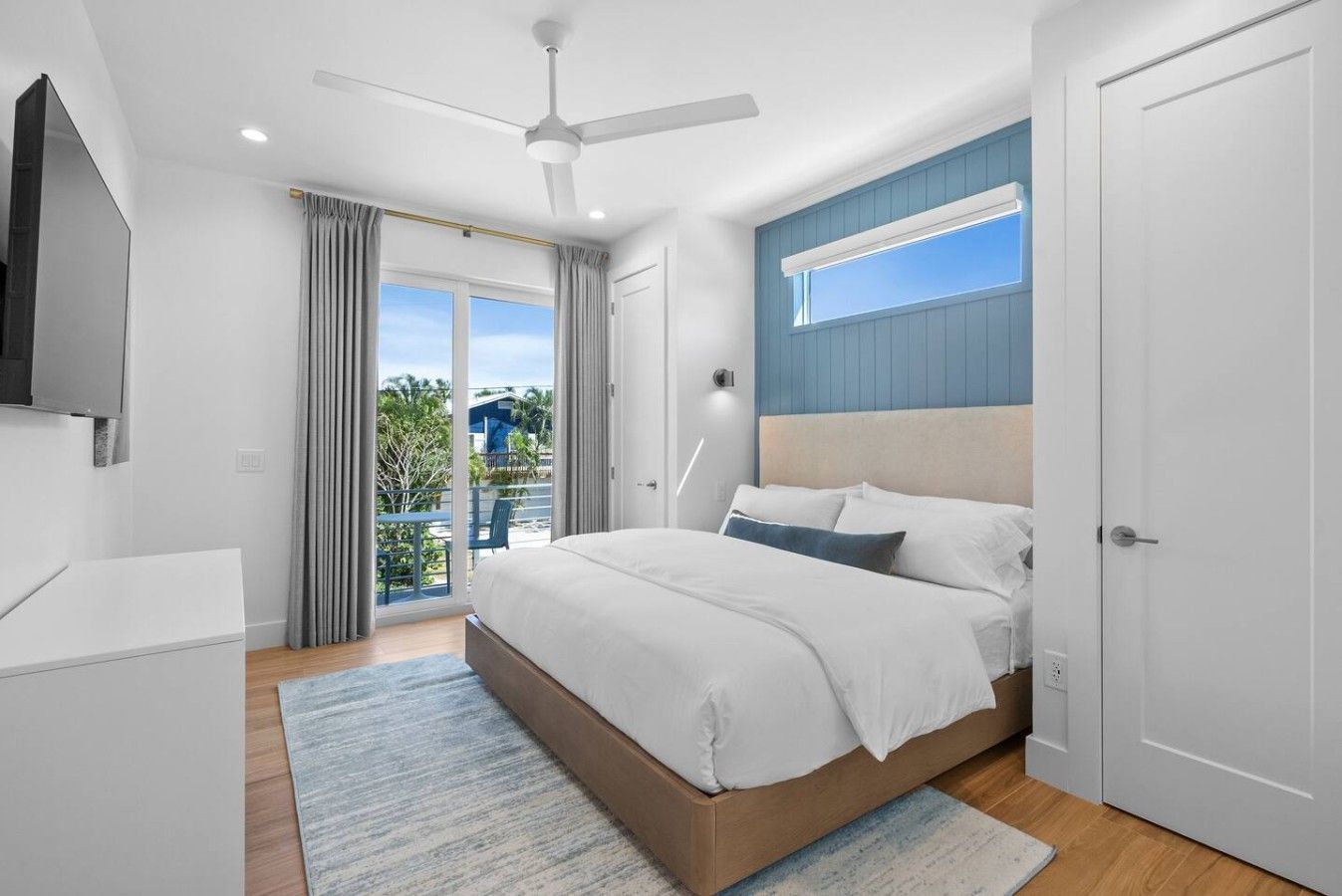 A modern bedroom with a bed, a ceiling fan, a TV, and a balcony with curtains.
