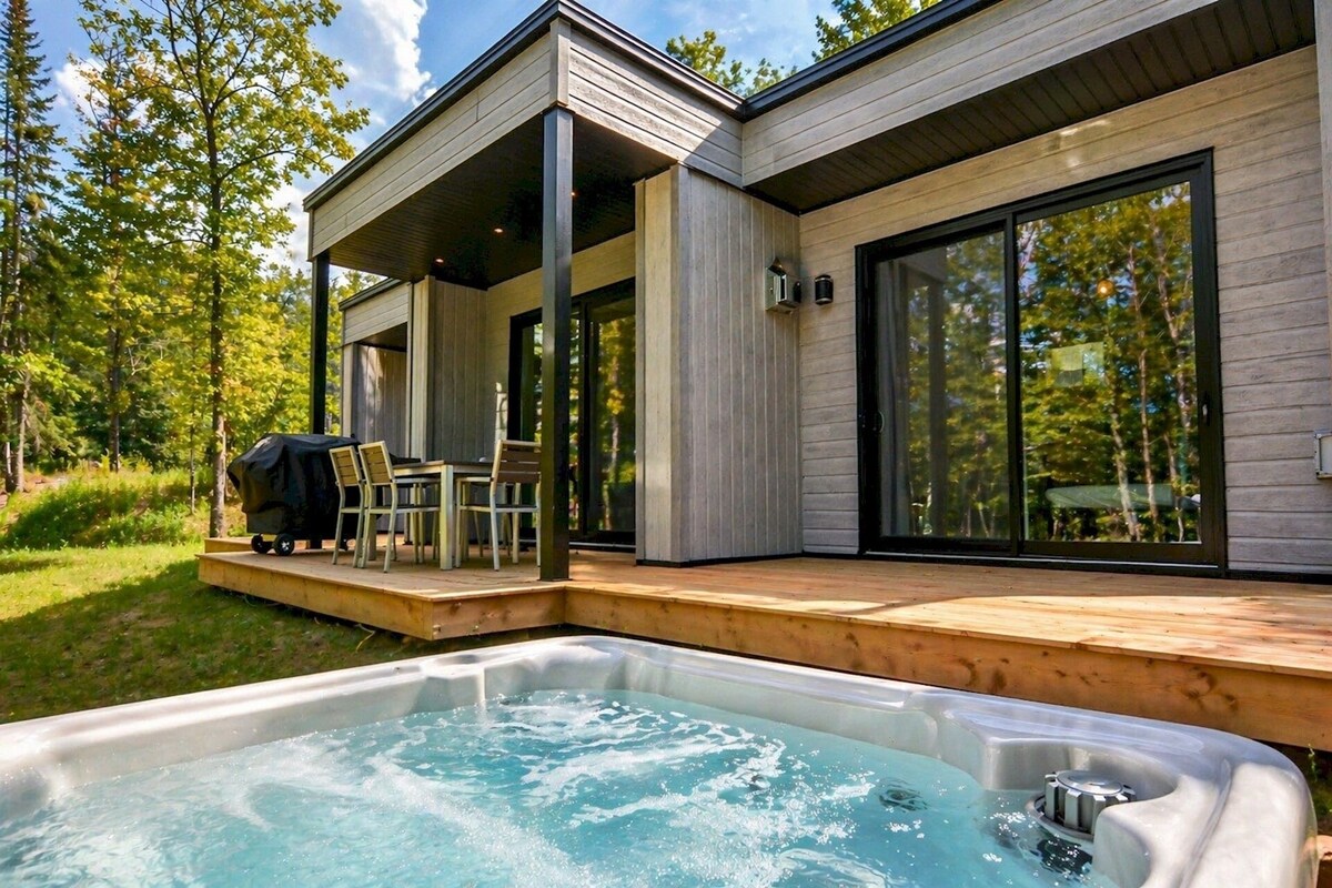 A modern outdoor hot tub area with a wooden deck, a covered patio, and a dining set.