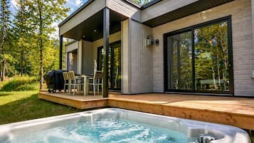 Un espace moderne aménagé à l’extérieur avec un bain à remous, une terrasse en bois et un patio couvert, ainsi qu’un ensemble de mobilier de jardin.